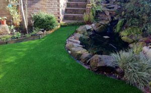 Superior artificial grass installed around stone work in a garden